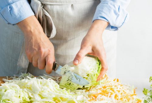 Woman slices fresh organic cabbage for making salad or for salting cabbage natural background. Processing of the autumn harvest. Vegetarian healthy food concept. Horizontal frame